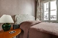 a queen-size bed with wooden bedside table, and a stylish lamp in paris luxury apartment