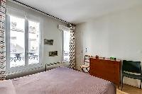 master bedroom with bright windows, a queen-size bed, a wooden closet and two seats in paris luxury 