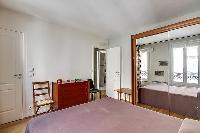 bedroom with a large wooden wardrobe closet with a full-length mirror placed beside the bed in paris