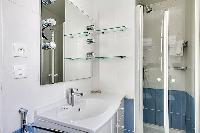 blue-tiled bathroom furnished with a shower area, a sink, a mirror, and a hairdryer in paris luxury 