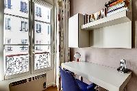 a desk with blue chair, a telephone, and selection of books beside the window in paris luxury apartm